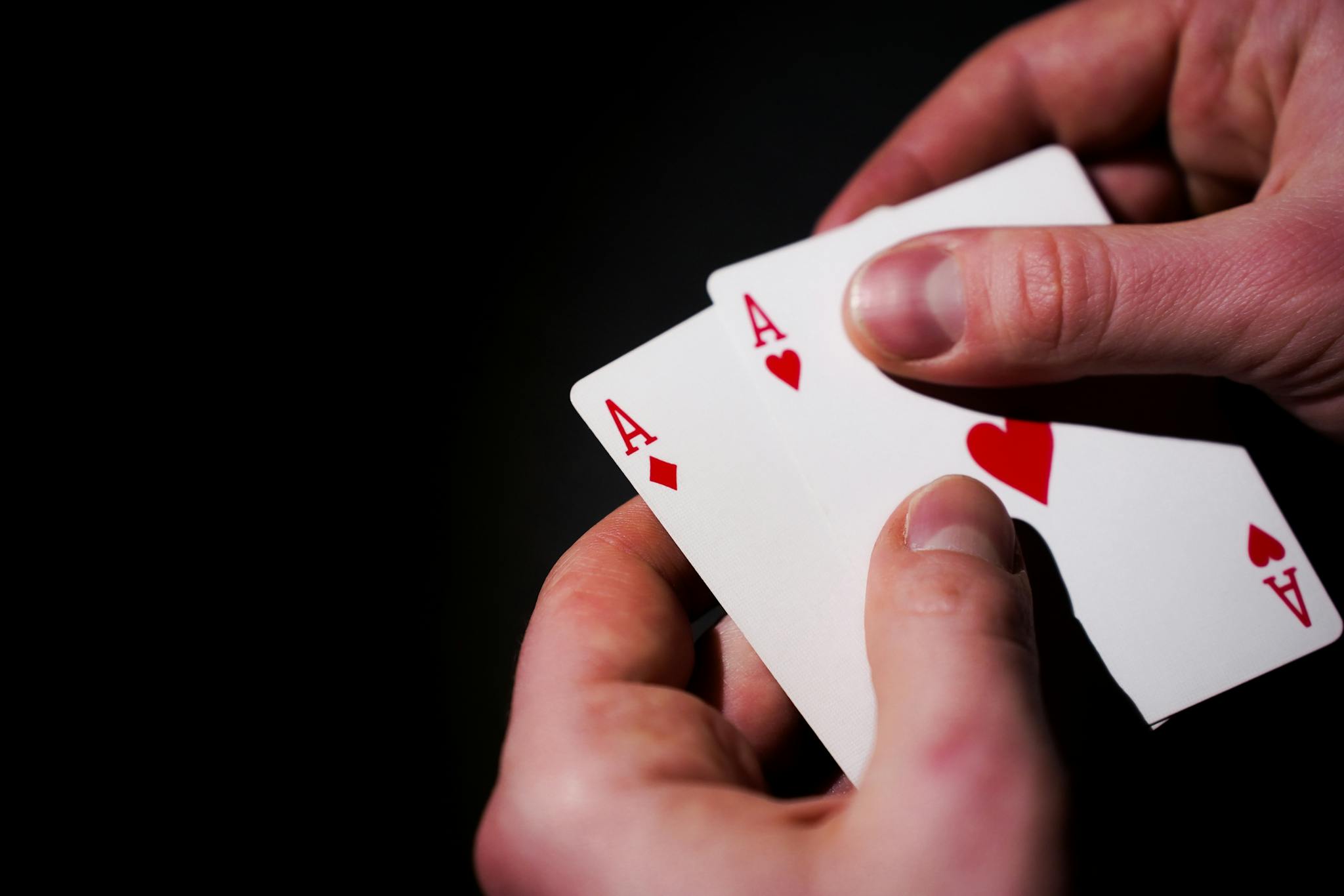 Hands holding three aces against a dark background, symbolizing luck and skill in card games.